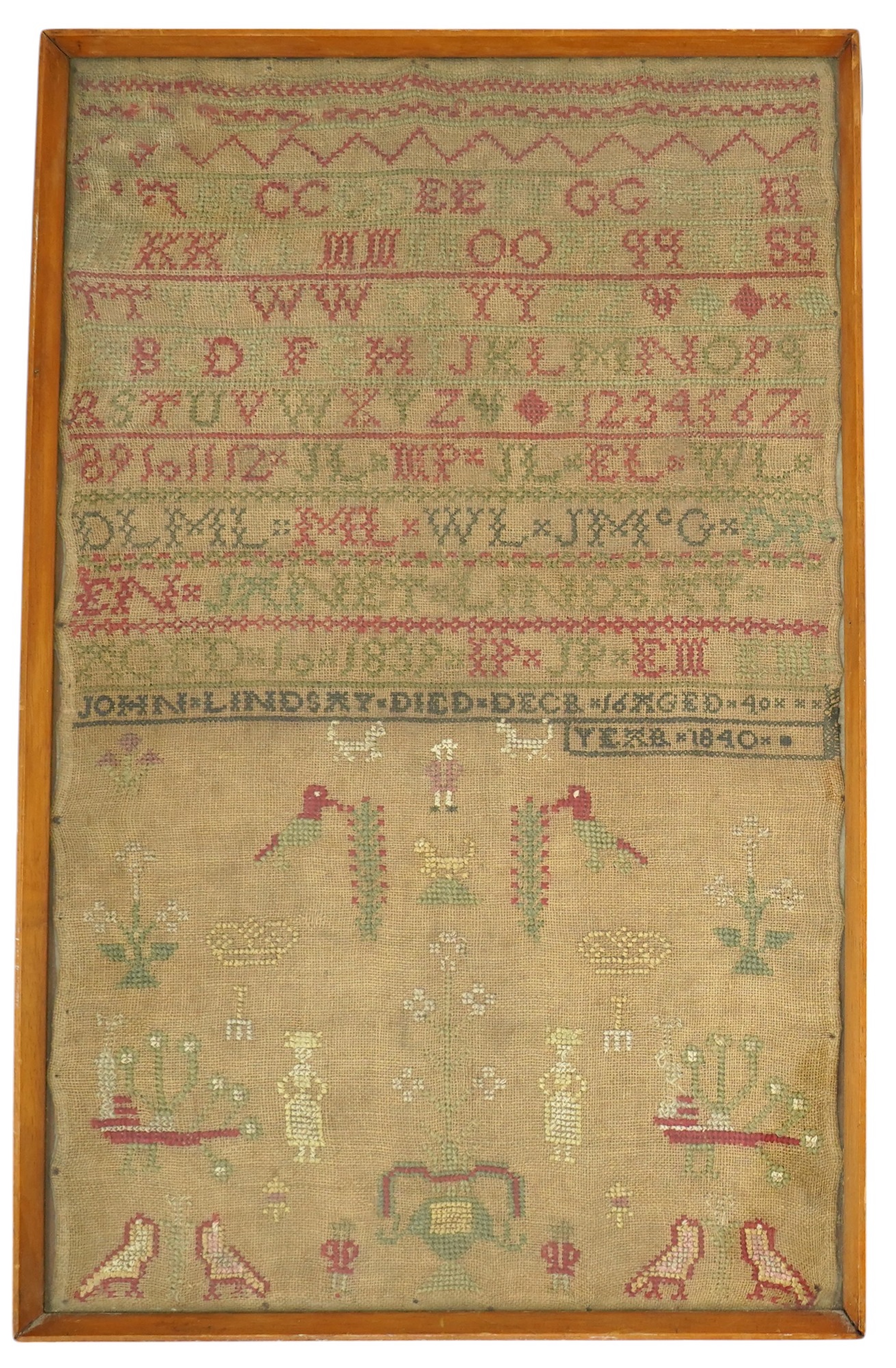 An alphabet cross stitch sampler with a figurative lower spot motif panel and commemorative dedication to John Lindsay, died Dec 16 1840, 27cm wide x 43.5 cm high. Condition - some light staining to linen, the blue and g